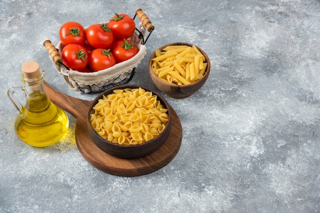 Holzschalen mit rohen verschiedenen Nudeln und frischen Tomaten auf Marmor.