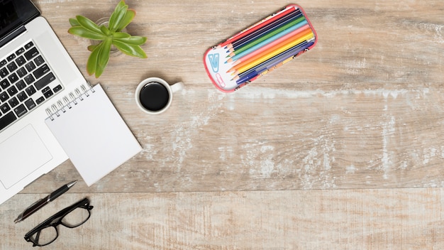 Holzschreibtisch mit geöffnetem Laptop; Tee; Brillen; Stift; Pflanzen und bunte Bleistifte