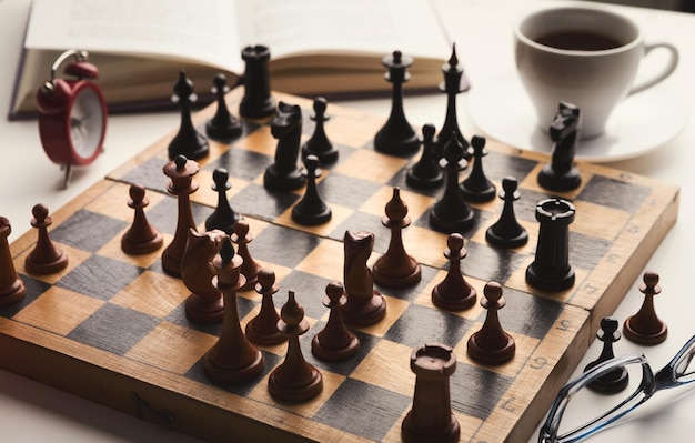 Holzschreibtisch mit schachspiel, buch und tasse kaffee auf weißem tisch. brettspiel-, intelligenz- und gehirn-upgrade-konzept