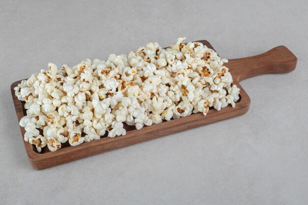 Holztablett mit einem Griff, der mit einer Portion Popcorn auf Marmortisch gefüllt ist.