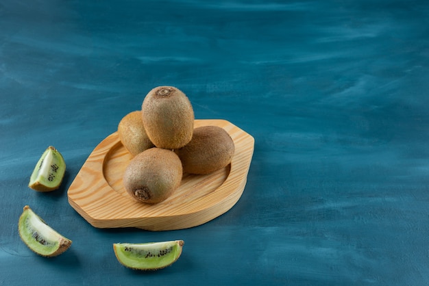 Holzteller mit frischen Kiwis auf Marmoroberfläche.