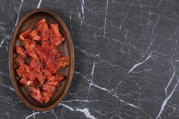 Holzteller mit geschnittenen Tomaten auf Marmor.
