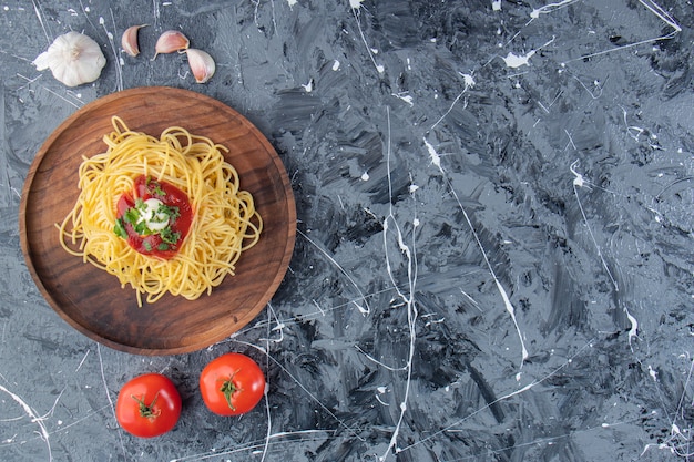 Holzteller mit leckeren spaghetti mit tomatensauce und gemüse auf marmoroberfläche.