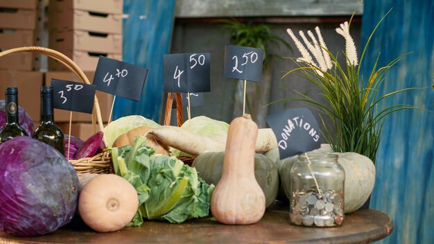 Kostenloses Foto holztisch mit saisonalem obst und gemüse, leerer stall mit münzen für spenden, leerer bauernmarkt mit organischen naturprodukten aus dem garten, handschuss.