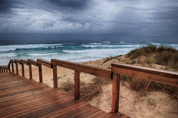 Holzweg am Strand durch die atemberaubenden Meereswellen unter dem bewölkten Himmel