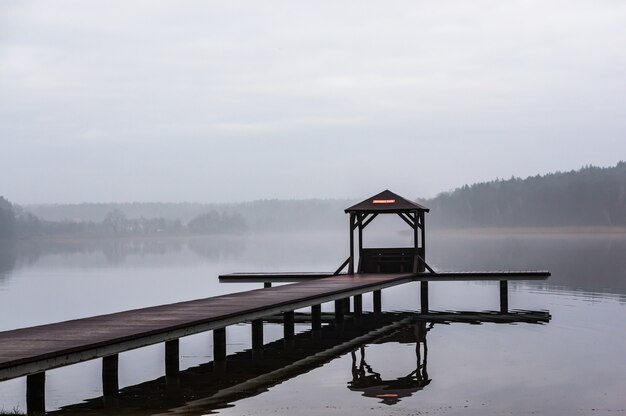 Holzweg über dem Wasser, umgeben von Bäumen mit nebligem Hintergrund