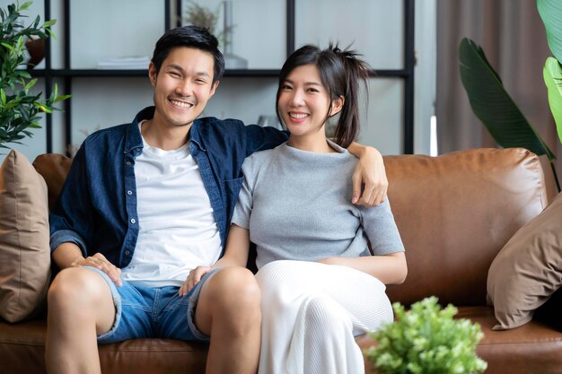 Home Isolation Konzept Glück asiatisches Liebespaar familygood Gespräch auf Sofa Couch im Wohnzimmer heiraten Paar lachen Lächeln zusammen auf dem Sofa