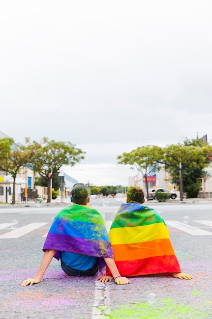 Kostenloses Foto homosexuell mit den regenbogenflaggen, die auf straße sitzen