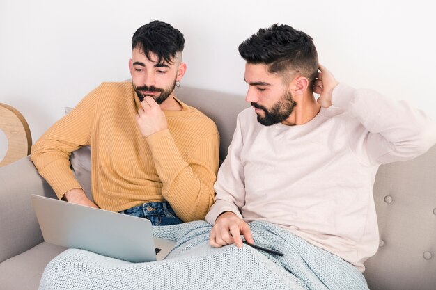 Homosexuelle Paare, die auf Sofa in einer Decke betrachtet Laptop sitzen