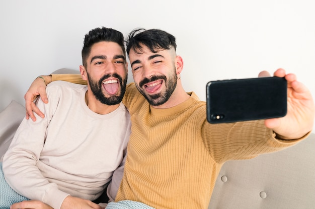 Homosexuelle Paare, die ihre Zunge beim Nehmen des Selbstporträts am intelligenten Telefon heraus haften