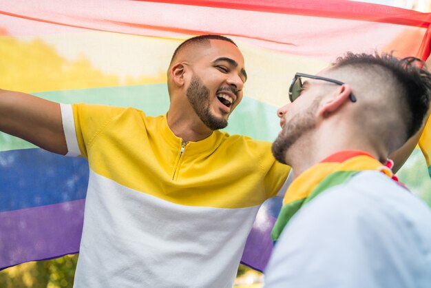 Homosexuelles Paar, das ihre Liebe mit Regenbogenfahne umarmt und zeigt.