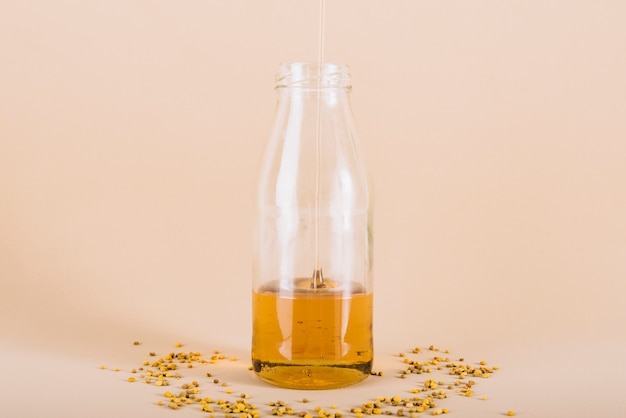 Honig, der in Glasflasche mit dem Bienenblütenstaub auf Pfirsich tropft, färbte Hintergrund