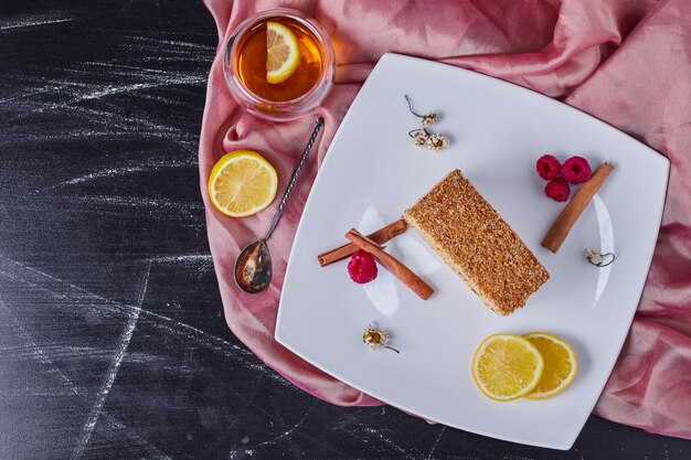 Honigkuchen auf weißem Teller mit Zimt, Zitrone und Beeren neben Teetasse.