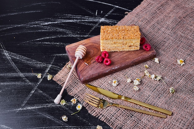 Honigkuchen mit Honiglöffel und Himbeeren auf dunklem Hintergrund.