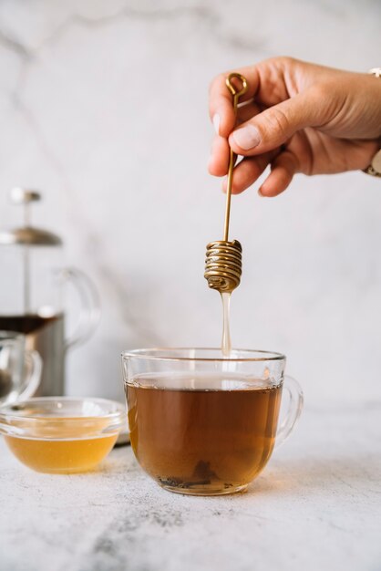 Honigstange über einer Tasse Tee, die in der Hand gehalten wird