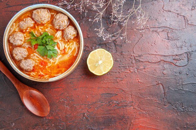 Horizontale Ansicht der Fleischbällchensuppe mit Nudeln in einer braunen Schüssel Zitronenlöffel auf der rechten Seite auf dunklem Hintergrund