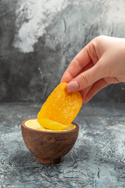 Kostenloses Foto horizontale ansicht der hand, die kartoffelchip in einer kleinen mayonnaise-schüssel auf grauem tisch hält