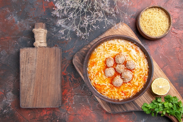 Horizontale Ansicht der leckeren Fleischbällchensuppe mit Nudeln an Bord von Zitronenholznudeln ein Bündel Grüns auf dunklem Hintergrund