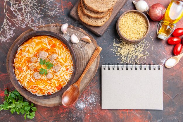 Horizontale Ansicht der leckeren Nudelsuppe mit Hühnchen auf Holzbrett Grüns Löffel Knoblauchtomate und Notebook auf dunklem Hintergrund