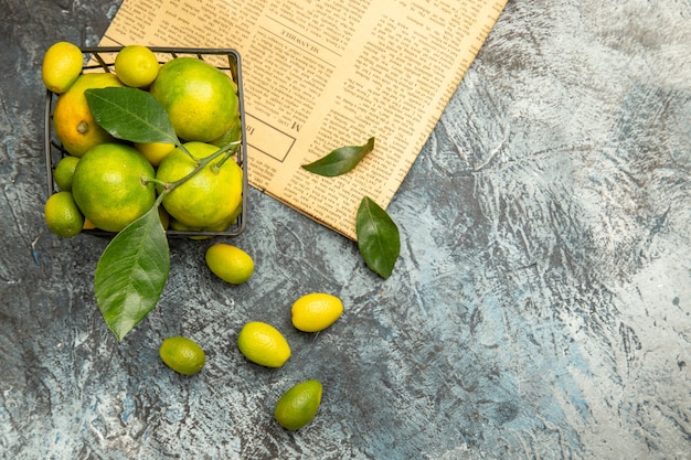 Horizontale Ansicht des schwarzen Korbes mit frischen grünen Mandarinen und Kumquats auf Zeitungen auf grauem Hintergrund stockbild