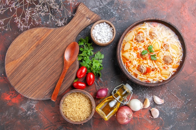 Horizontale Ansicht einer köstlichen Nudelsuppe mit Hühnchen auf einem Holzbrett, ein Haufen grüner Tomaten, Ölflasche auf dunklem Hintergrund