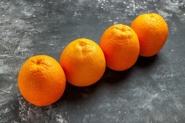 Horizontale Ansicht von drei natürlichen organischen frischen Orangen, die in einer Reihe auf dunklem Hintergrund aufgereiht sind