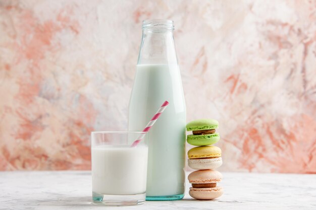 Horizontale Ansicht von frischer Milch in einer offenen Flasche und einer Glastasse neben bunten leckeren Macarons auf pastellfarbener Oberfläche