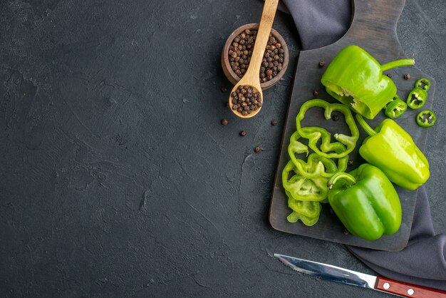 Horizontale Ansicht von ganzen geschnittenen gehackten grünen Paprika auf Holzbrett auf dunkler Farboberfläche