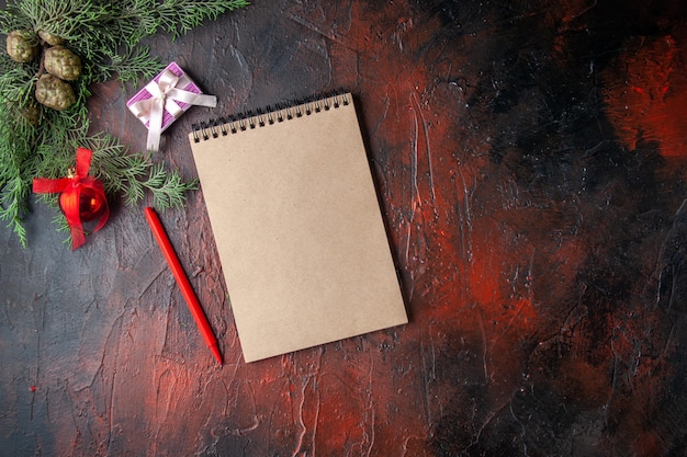 Horizontale Ansicht von Tannenzweigen mit Dekorationszubehör und Geschenk neben Notebook auf dunklem Hintergrund