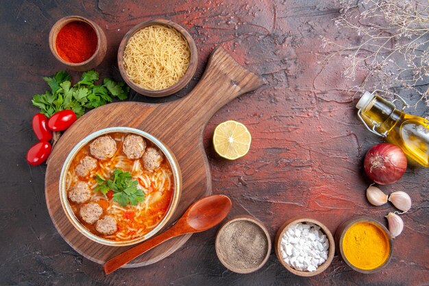 Horizontale Ansicht von Tomaten-Fleischbällchen-Suppe mit Nudeln in einer braunen Schüssel und verschiedenen Gewürzen Ölflasche Zwiebel Knoblauch auf dunklem Hintergrund