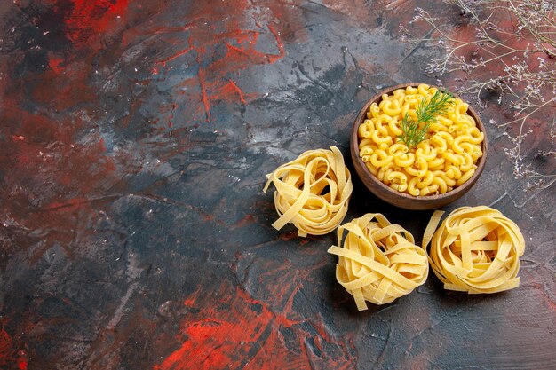 Horizontale Ansicht von ungekochten drei Portionen Spaghetti und Schmetterlingsnudeln in einer braunen Schüssel und Grün auf der linken Seite der gemischten Farbtabelle