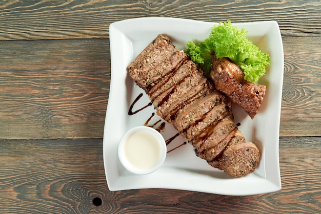 Horizontale Aufnahme der Draufsicht von geschnittenem Fleisch auf einem weißen quadratischen Teller auf dem hölzernen Tisch copyspace, der Nahrungsmittelrezept Abendessen Mahlzeit Mittagessen Abendessen geröstete Soßengrüns verziert.