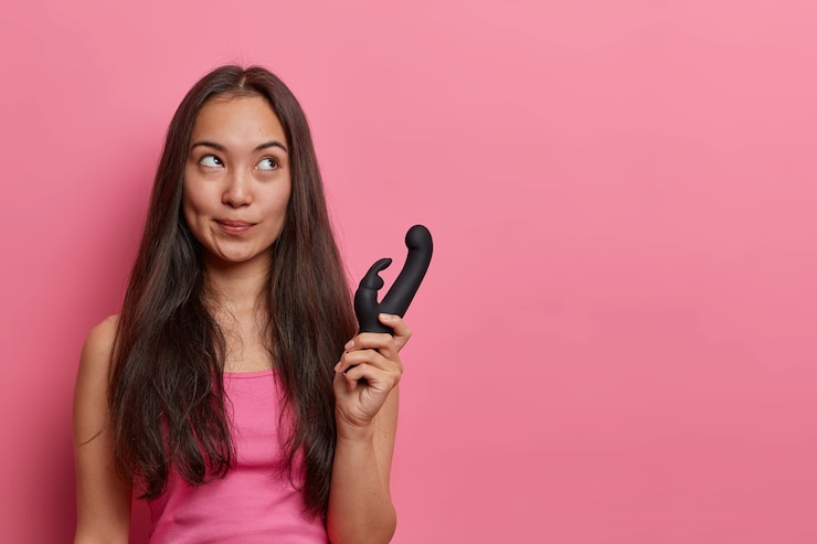 Kostenlose Foto horizontale aufnahme der nachdenklichen asiatischen frau hält kaninchen geformten vibrator, verwendet erotisches spielzeug zum vergnügen, kauft vibrierendes sexspielzeug für erwachsene, erhält entspannung und vergnügen. vaginales trainingsgerät