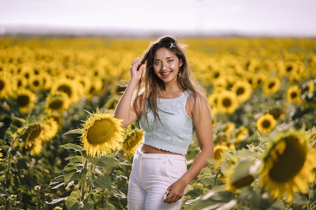Horizontale Aufnahme einer kaukasischen jungen Frau, die in einem hellen Feld von Sonnenblumen an einem sonnigen Tag aufwirft