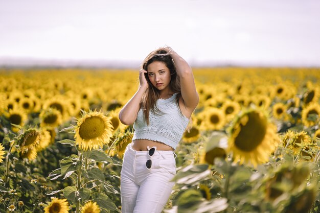 Horizontale Aufnahme einer kaukasischen jungen Frau, die in einem hellen Feld von Sonnenblumen an einem sonnigen Tag aufwirft