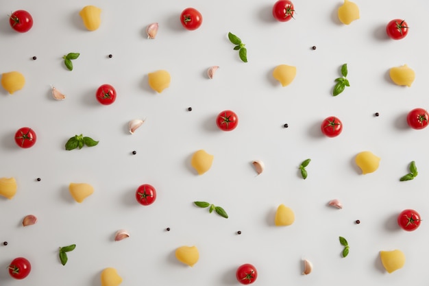 Horizontale Aufnahme von Bio-Muschelmakkaroni mit aromatischen leckeren italienischen Kräutern und Gewürzen, frischem reifem Gemüse zum Kochen von Nudeln, weißem Hintergrund. Gesunder Energielebensstil. Vegetarisches Gourmetgericht