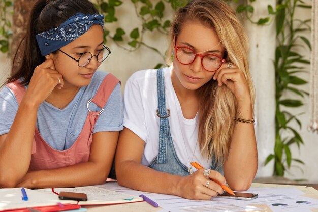 Horizontale Aufnahme von Studenten oder Kollegen, die sich über ein gemeinsames Projekt unterhalten, Papiere betrachten, Notizen im Notizblock machen und Stift halten