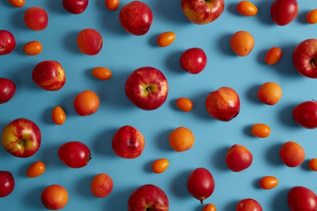 Horizontale Aufnahme von süßen saftigen roten Äpfeln, Pfirsichen, Tamarillo, Cumquat auf blauem Hintergrund. Leckere Früchte. Sammlung von gesunden Lebensmitteln oder verschiedenen Arten von Obst aus biologischem Anbau. Sommerdiätkonzept