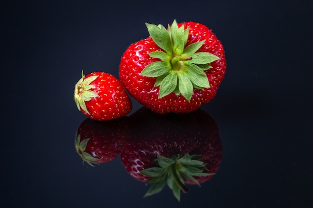Horizontale Aufnahme von zwei roten kroatischen Erdbeeren auf einer schwarzen reflektierenden Oberfläche