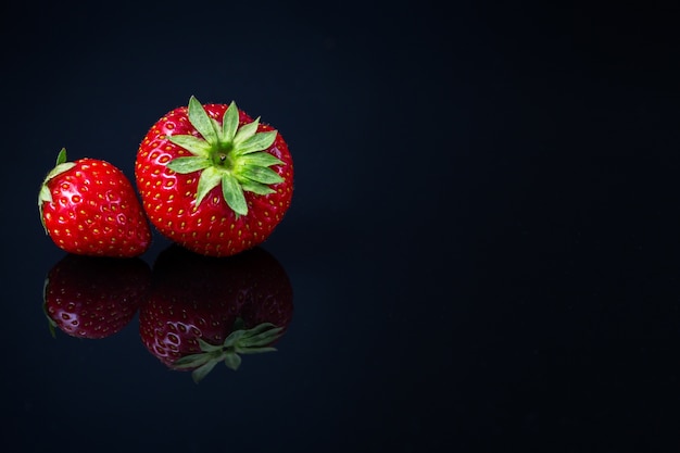Horizontale Aufnahme von zwei roten kroatischen Erdbeeren auf schwarzer reflektierender Oberfläche - Raum für Ihren Text