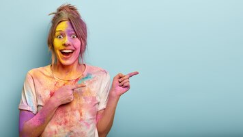 Horizontale studioaufnahme der glücklichen europäischen frau zeigt zur seite, bedeckt mit holi-farben