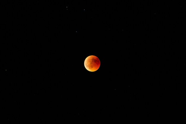 Horizontaler langer Schuss eines orange und roten Mondes im dunklen Himmel bei Nacht