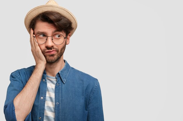 Horizontaler Schuss des nachdenklichen verwirrten bärtigen Mannes hält Hand auf Wange