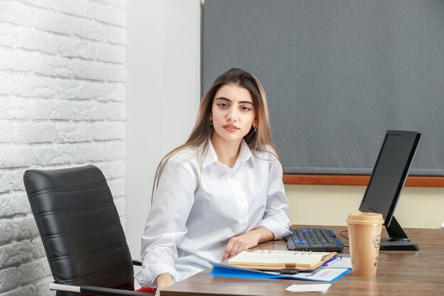 Horizontales Foto einer jungen Geschäftsfrau, die hinter dem Schreibtisch sitzt und in die Kamera schaut