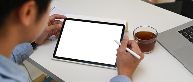 Horizontales foto eines geschäftsmannes, der ein digitales tablet mit leerem bildschirm hochhält, während er am schreibtisch sitzt.