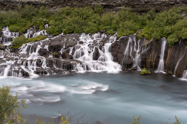 Hraunfossar Wasserfälle, die tagsüber von Grün in Island umgeben sind