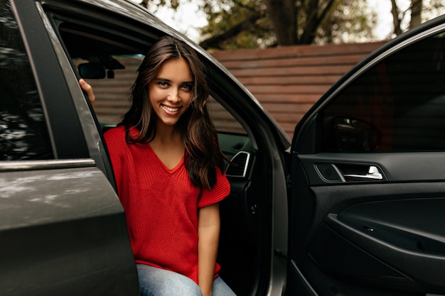 Kostenloses Foto hübsch lächelnd lag mit langen gewellten haaren im roten hemd und lächelte lächelnd im auto