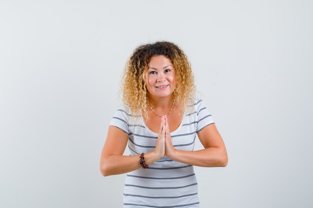 Kostenloses Foto hübsche blonde frau, die namaste-geste im gestreiften t-shirt zeigt und lustig schaut. vorderansicht.