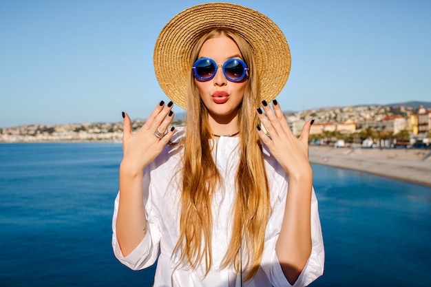 Hübsche blonde frau, die trendigen strohhut und blaue sonnenbrille trägt