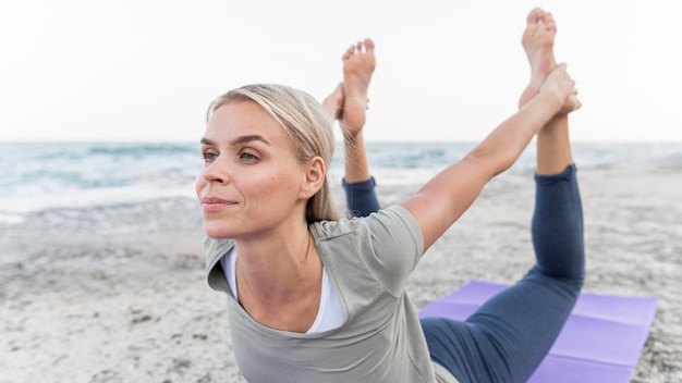 Hübsche blonde Frau, die Yoga am Strand tut